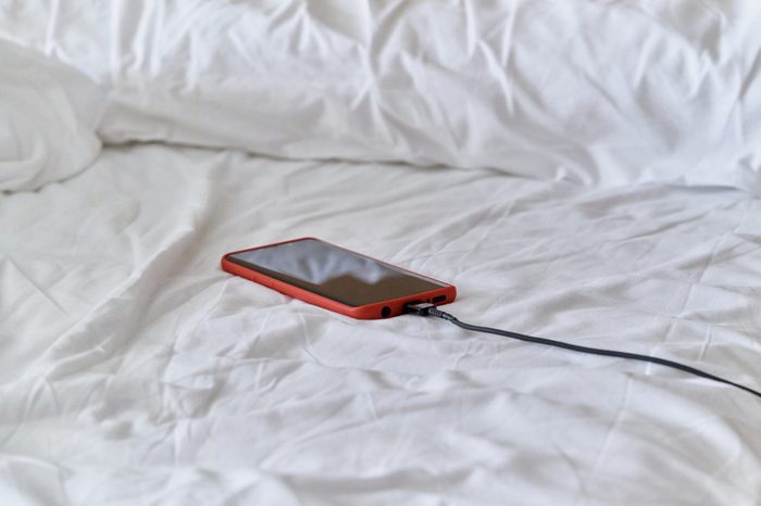 cell phone left charging on a bed of pillows and white blanket in the bedroom with the able facing the wall