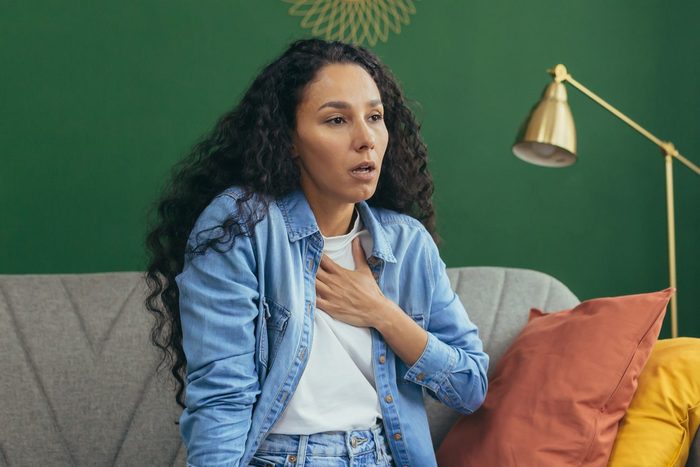 Woman having panic attack, Hispanic woman with curly hair alone at home depressed, having trouble breathing sitting on sofa in living room