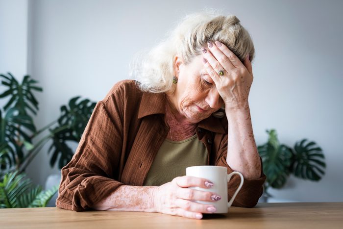 Upset senior woman with head in hand sitting at home