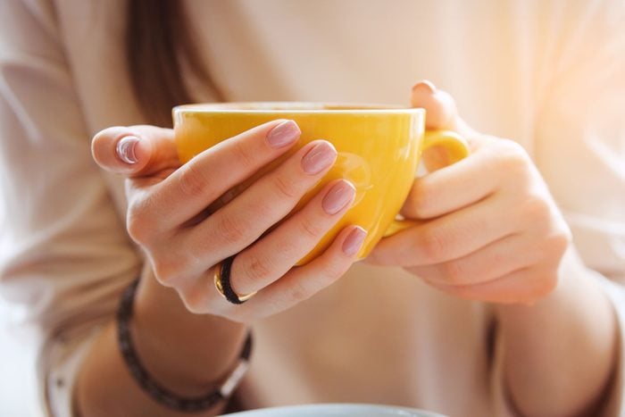 woman's hands holding a yellow tea cup