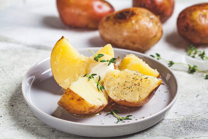 Baked potatoes with butter and thyme on gray plate.