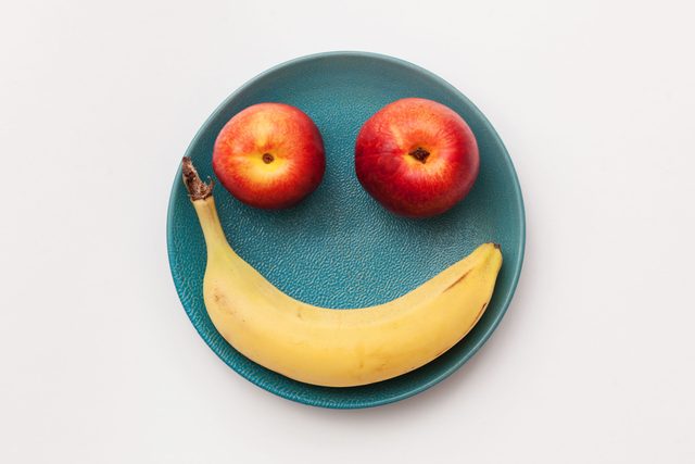 smiley face on a teal plate made from two apples for the eyes and a banana for the mouth