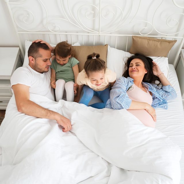 family of four in bed together. Two kids, a mom and a pregnant mom