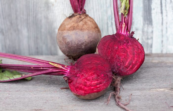 two red table beets, one cut in half, the other whole, on a wooden background close-up