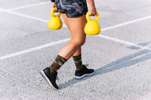 Young woman holding kettlebells while walking on road