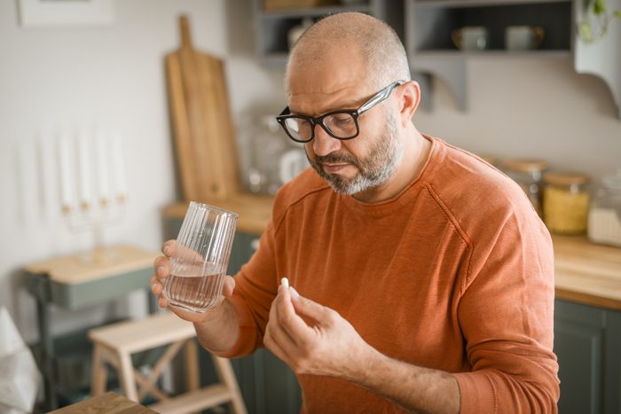 Mature adult man in cozy interior of home kitchen taking medication