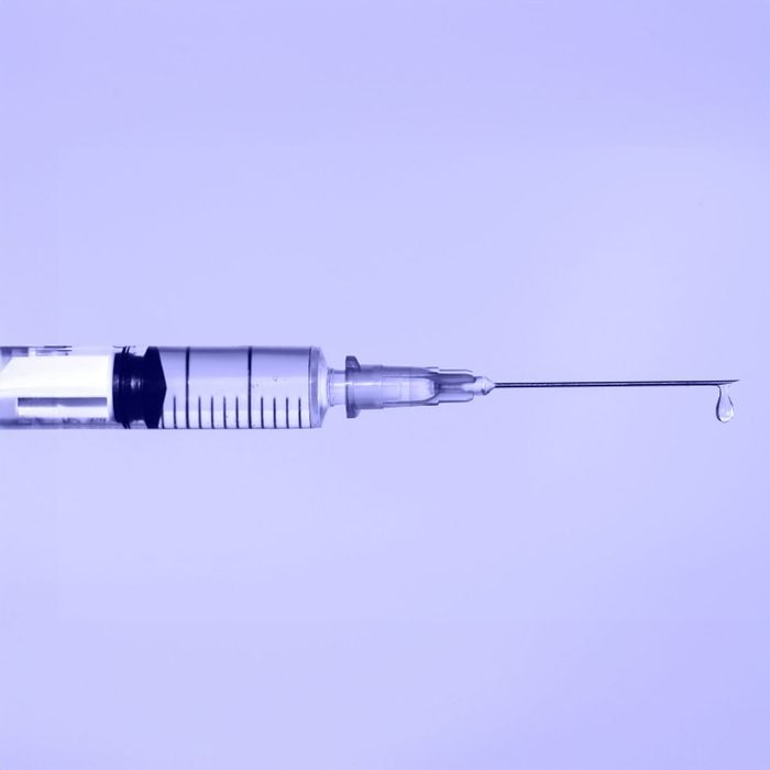 Botox syringe with drop of fluid on a purple background
