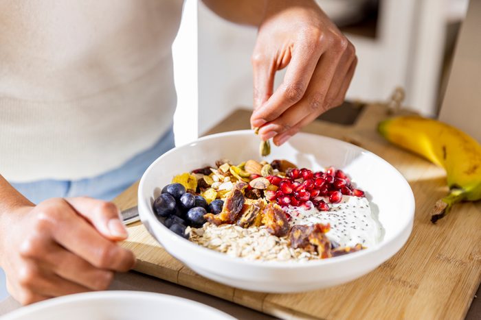 young woman is preparing her own bowl with fruits and nuts for breakfast