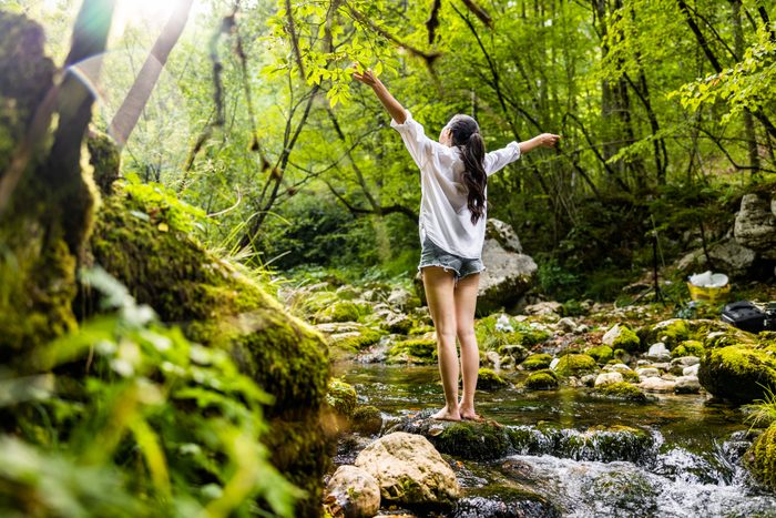 Woman with arms outstretched standing on rock amidst river