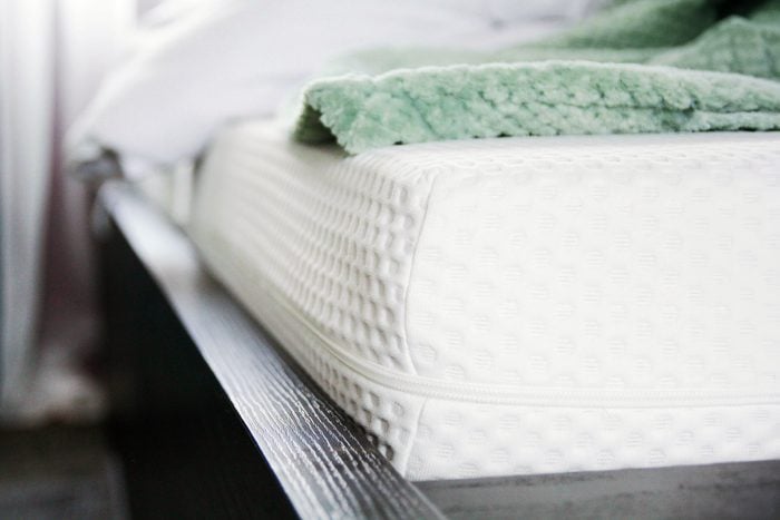 close up of a bare mattress in a bedroom with a green blanket rolled up in the background