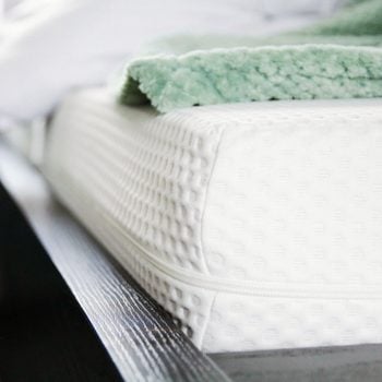 close up of a bare mattress in a bedroom with a green blanket rolled up in the background