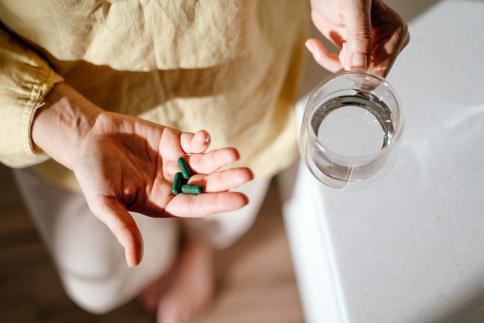 A woman standing at a table with green pills in her hand