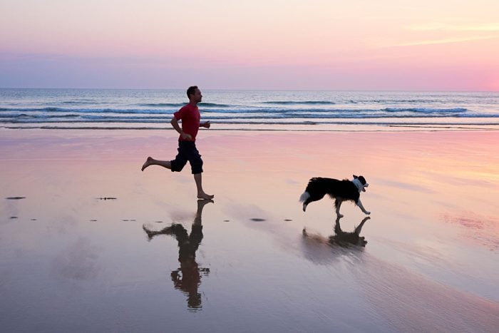 man running during sunrise on the beach with his border collie dog